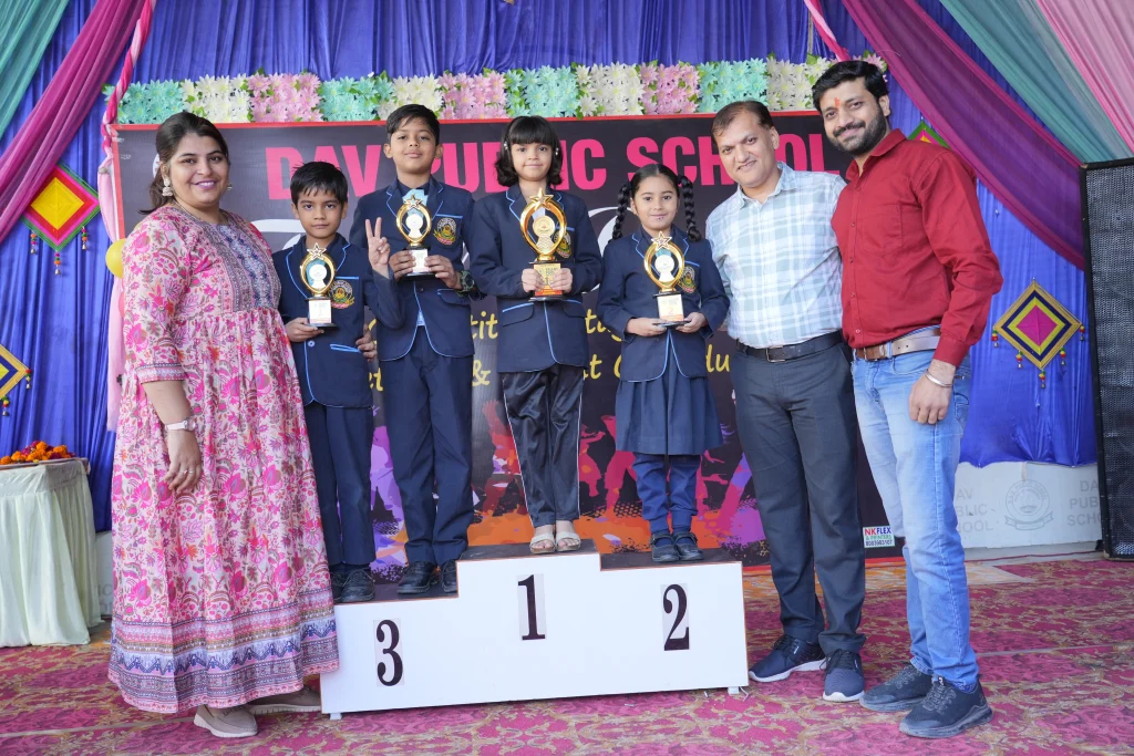 Prize-winning students of D.A.V. Public School Suratgarh standing on podium with trophies and teachers – Academic excellence at the Best School in Suratgarh